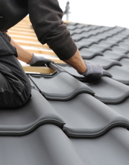 Couvreur installant des tuiles de toiture noires (profil double vague). Pose minutieuse sur l'ossature en bois lors du chantier.