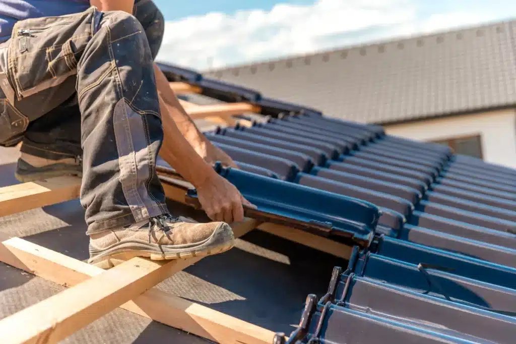couvreur professionnel installant des tuiles en céramique noire sur une charpente en bois, illustrant les travaux de couverture et l'expertise artisanale en rénovation de toiture ​​







