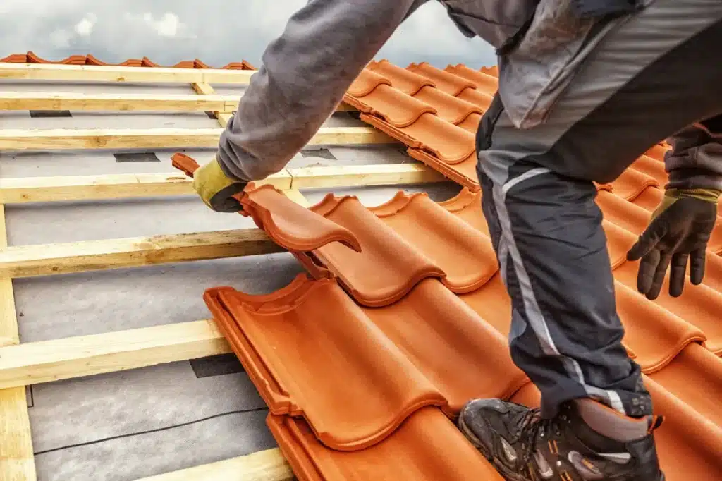 artisan couvreur posant des tuiles en terre cuite sur une charpente en bois, illustrant la rénovation et la réfection de toiture avec des matériaux traditionnels