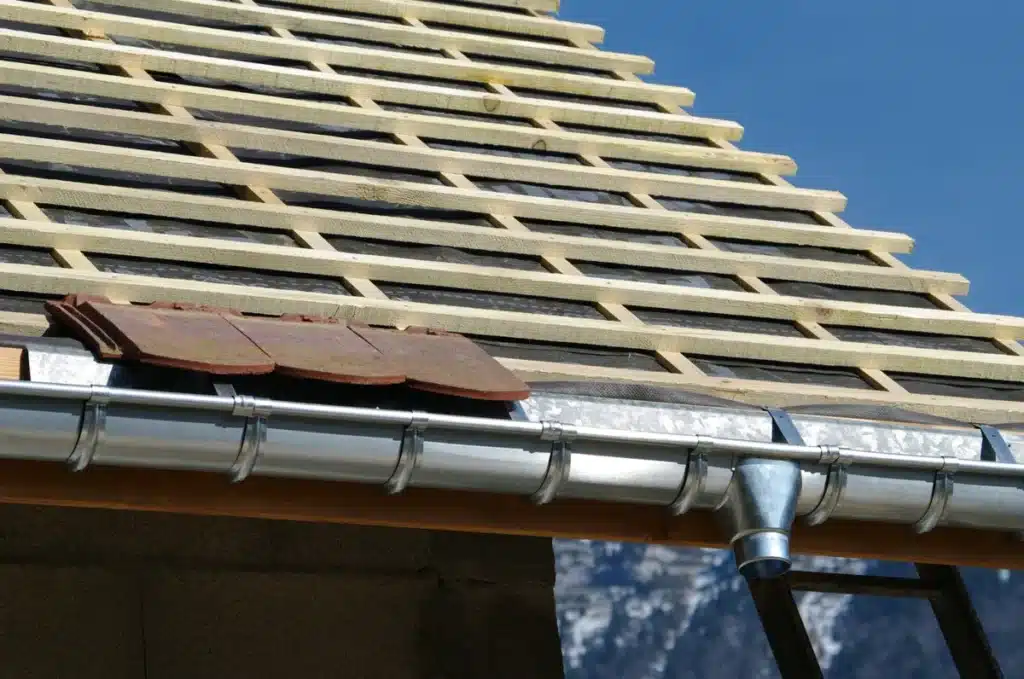 installation d'une zinguerie en bord de toiture avec gouttières métalliques et liteaux en bois, illustrant les travaux de couverture et d'évacuation des eaux de pluie ​​